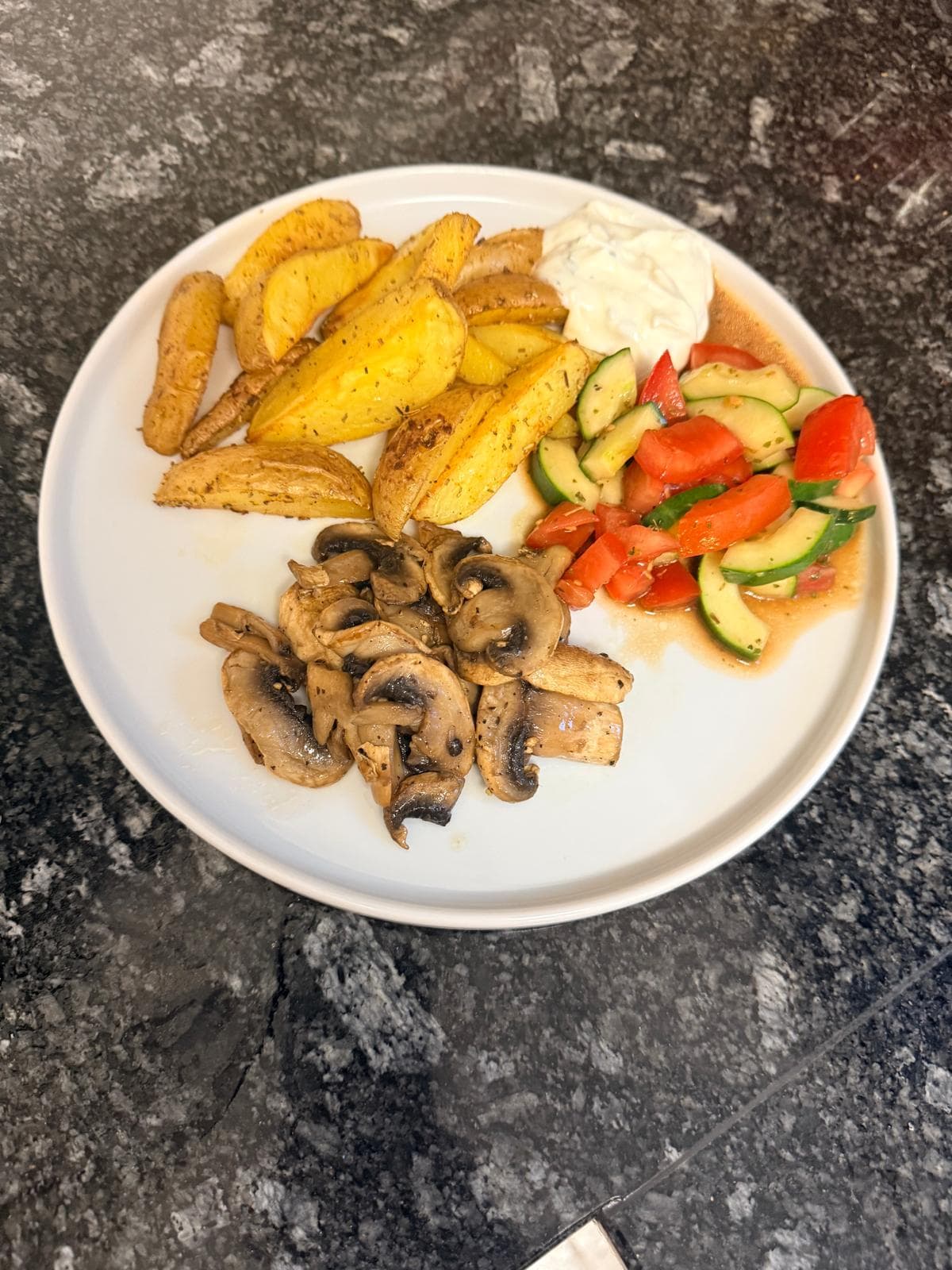Knusprige Ofenkartoffeln mit gebratenen Champignons, Tomaten-Gurken-Salat und cremigem Kräuterquark auf einem Teller
