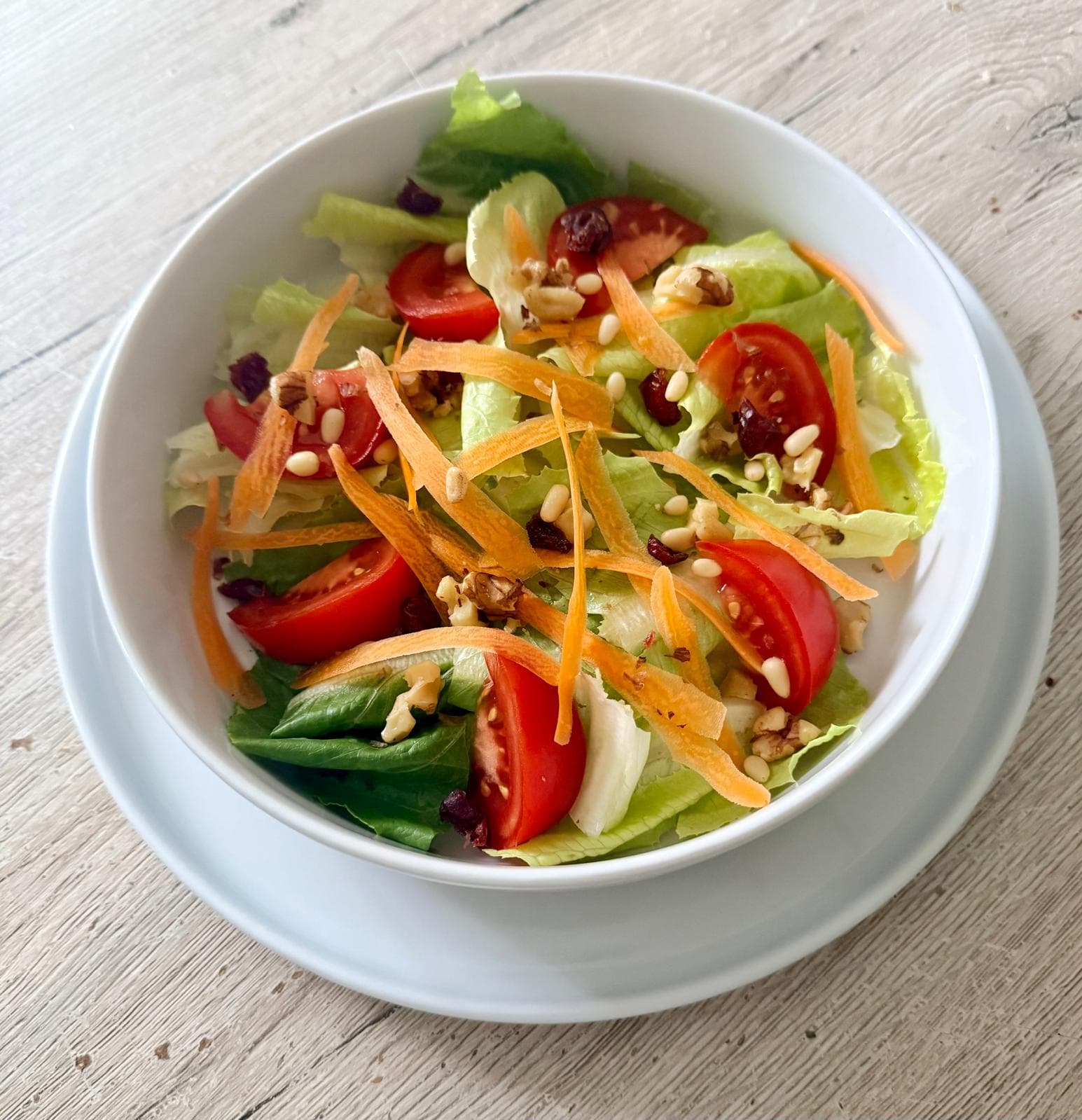 Bunter Blattsalat mit Tomatenstücken, feinen Rüeblistreifen, Baumnüssen, Pinienkernen und getrockneten Cranberries in einer Salatschüssel.