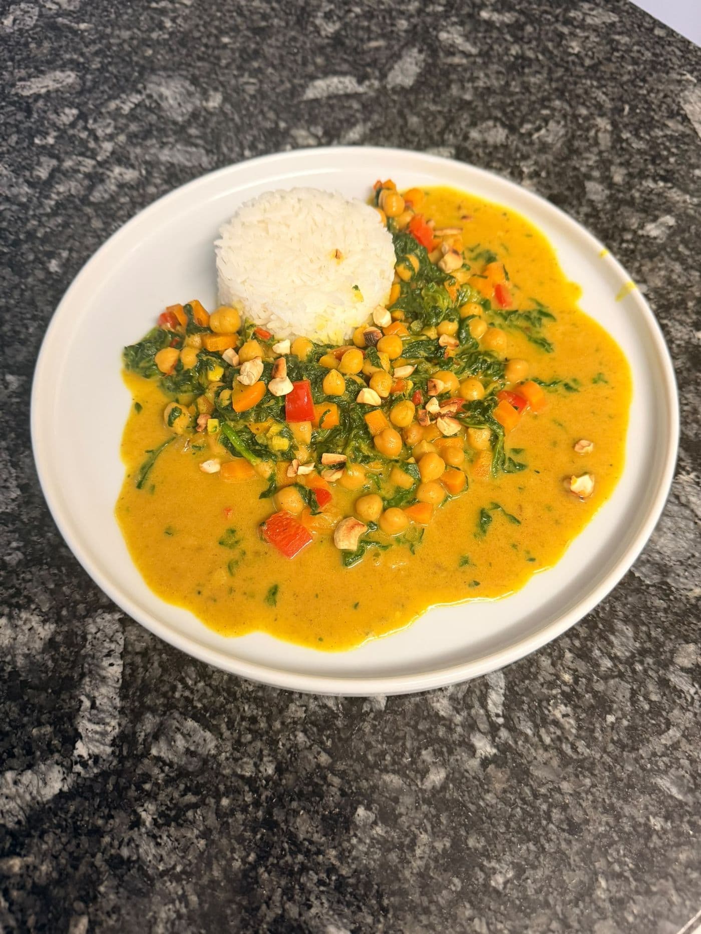 Weisser Teller mit cremigem Kichererbsen-Kokos-Curry mit Blattspinat und Gemüse.
