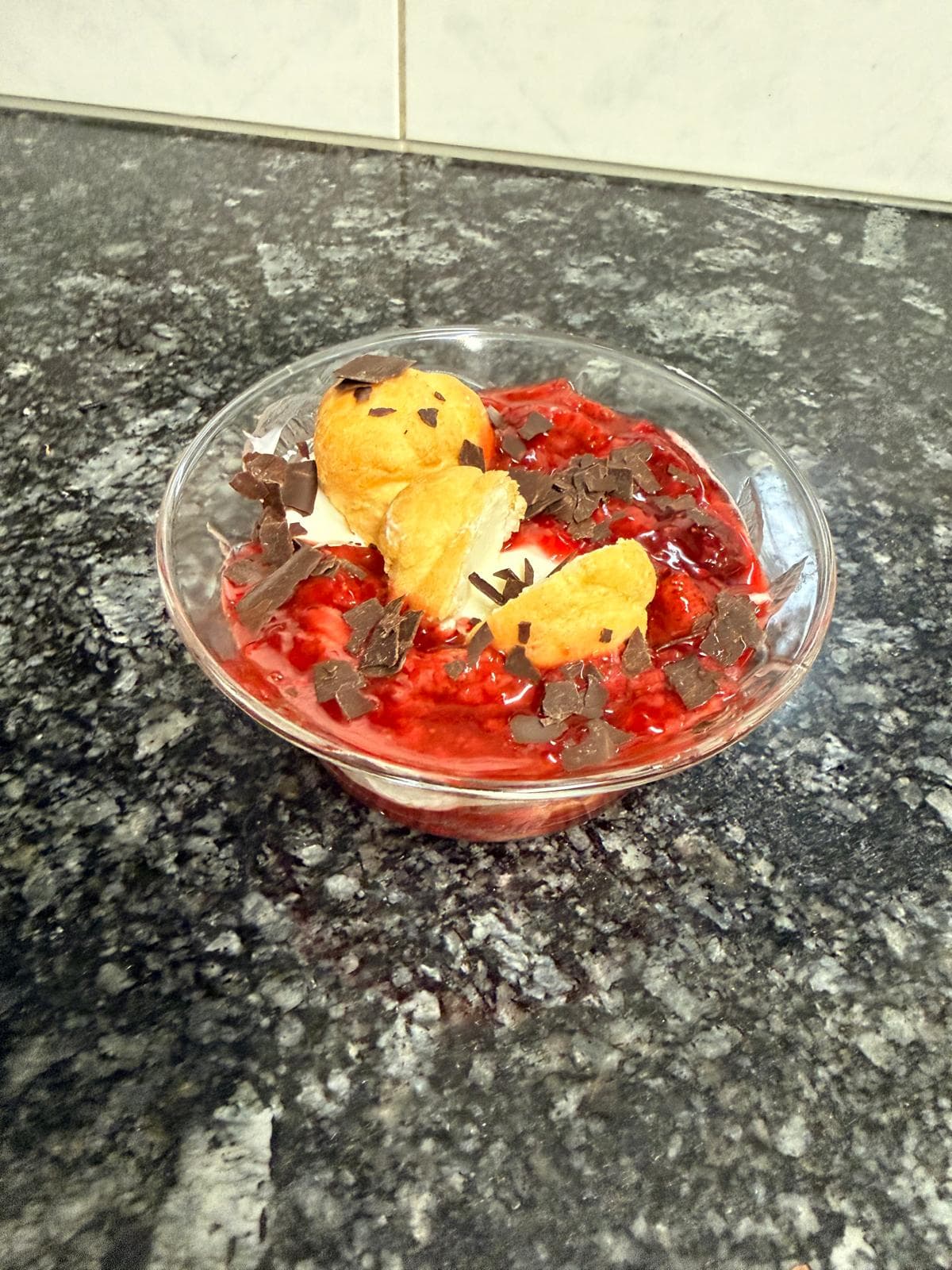 Luftiges Windbeutel-Dessert mit Erdbeer-Himbeer-Sauce, Mascarpone-Joghurtcreme und dunklen Schokoladenspänen in einer Dessertschale.