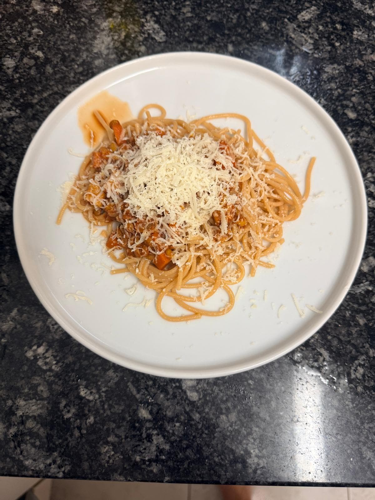 Proteinreiche Spaghetti mit Linsen-Bolognese, Gemüse und frisch geriebenem Käse auf einem weissen Teller.